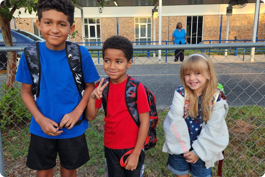 three kids standing in front of chainlink fence with backpacks on